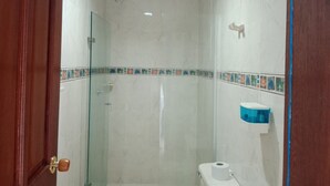 Un baño con cabina de ducha de vidrio, inodoro y un jabonero azul en la pared.