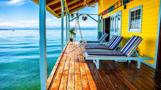 A wooden deck with two lounge chairs and a hammock, overlooking a body of water.