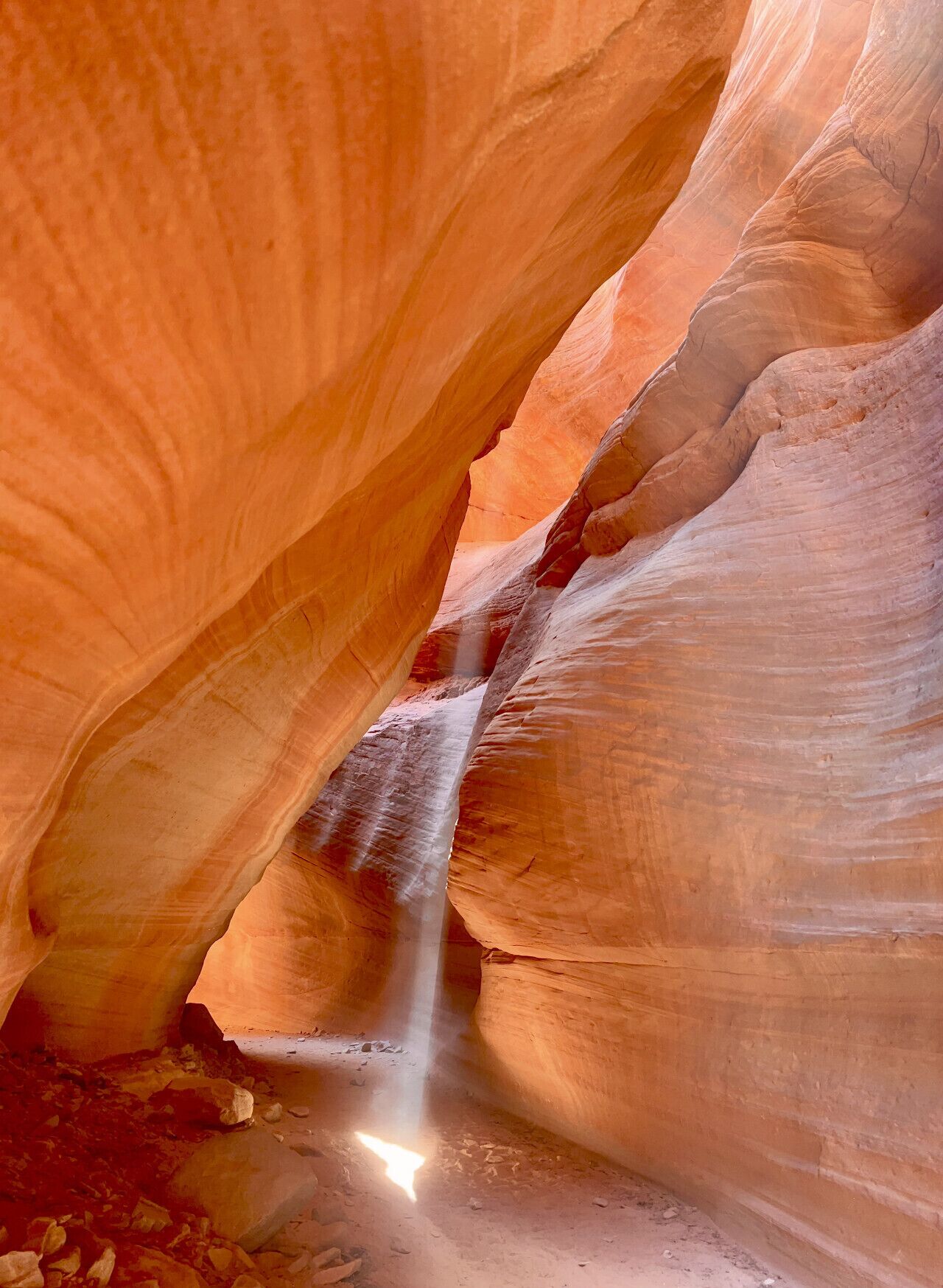 A narrow canyon with smooth, curved rock walls and a small stream flowing through it.