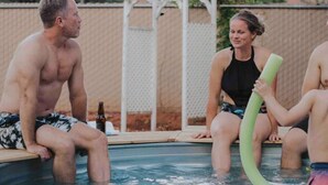 Ein Poolbereich mit einer Pergola, einer Flasche und Personen, die am Pool sitzen.