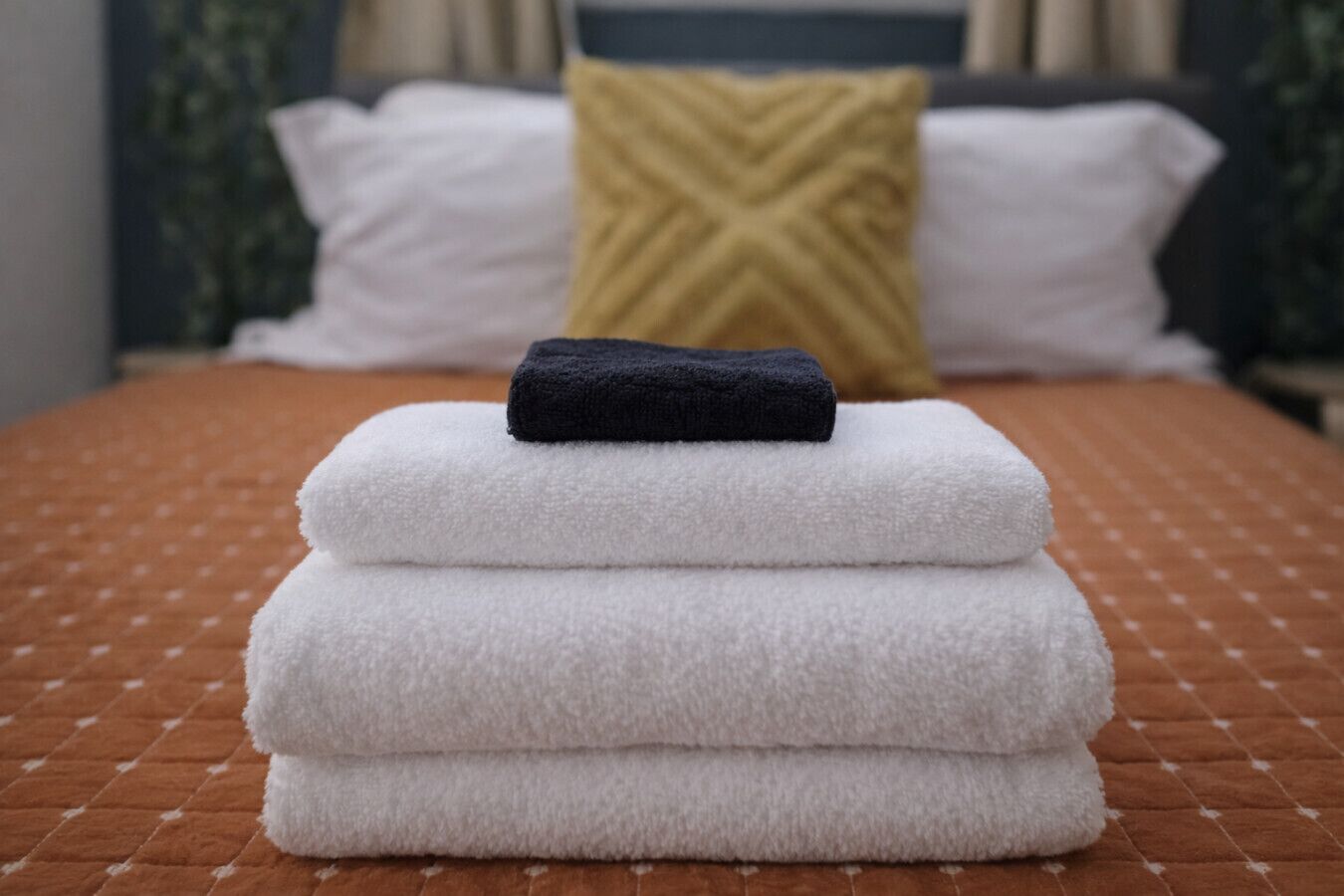 A neatly stacked set of towels on a bed with a patterned bedspread.