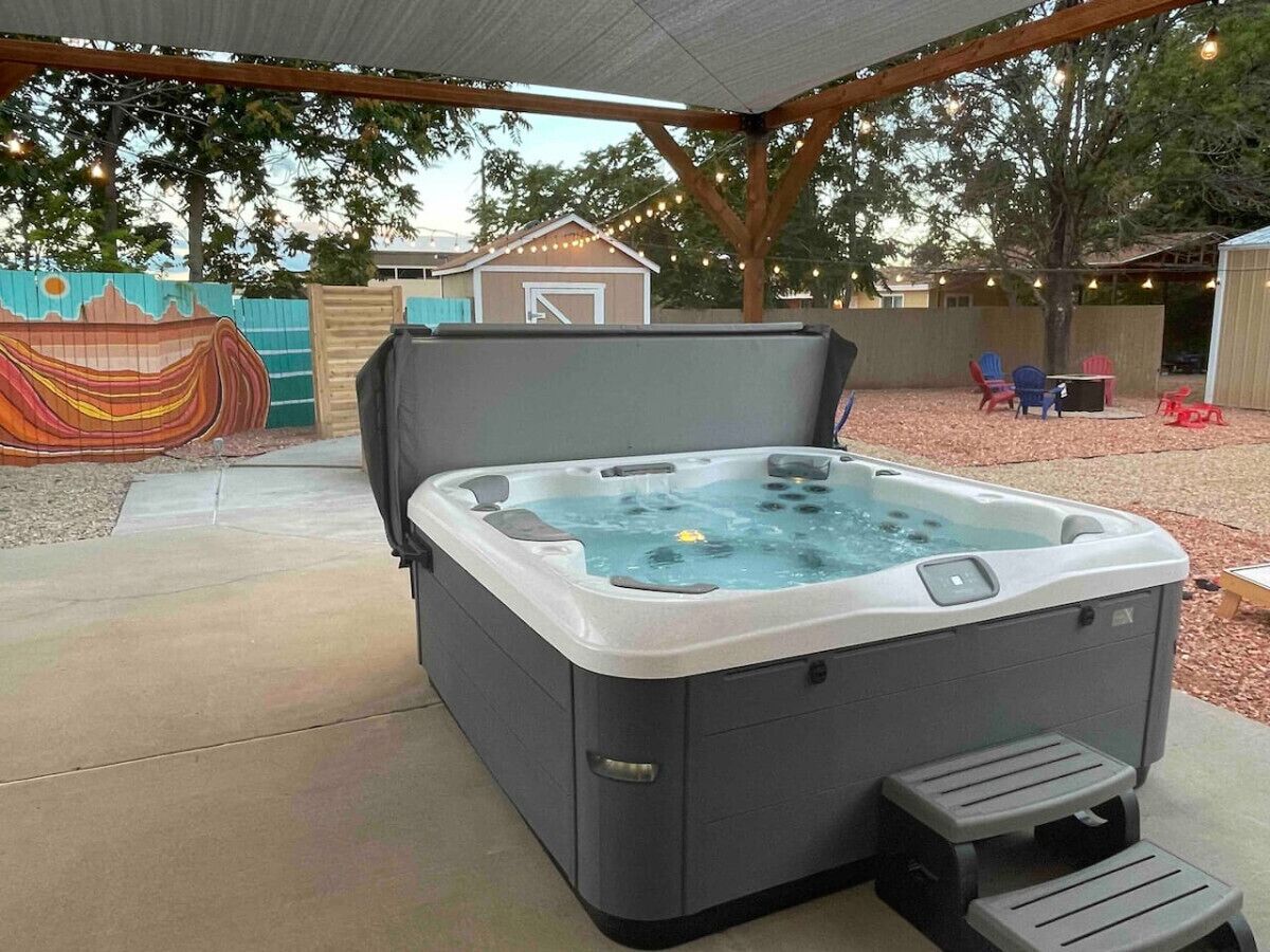 Un jacuzzi en un patio al aire libre con techo cubierto, una terraza de madera y un mural colorido de fondo.