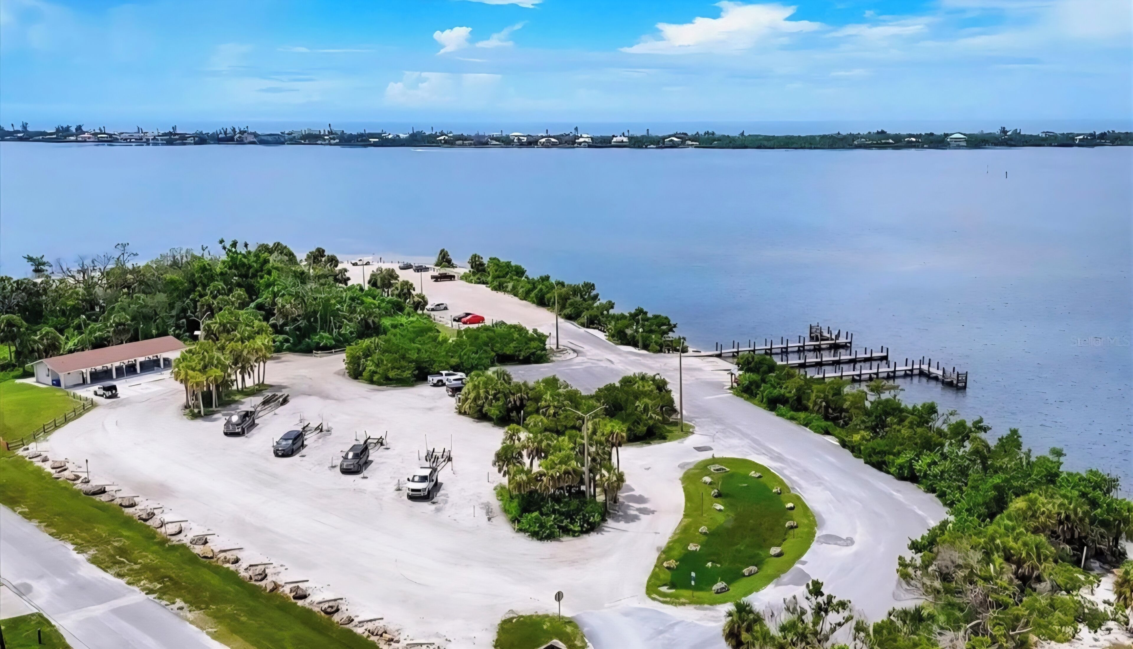 A coastal parking area with a building, vehicles, and a dock.