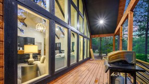 A wooden deck with large windows, a fireplace, and a view of the forest. - Campfire Dreams: Arcade, Hot Tub, Playset, 3BD/3Bath, Pet Friendly (Broken Bow)