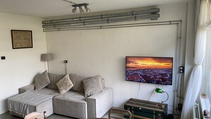 En stue med en modulsofa, et fladskærms-tv ophængt på væggen, et træbord og en vintageskuffe.