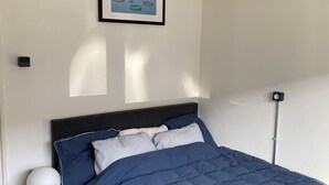 Et soveværelse med seng, sengebord, lampe og et billede i ramme på væggen.