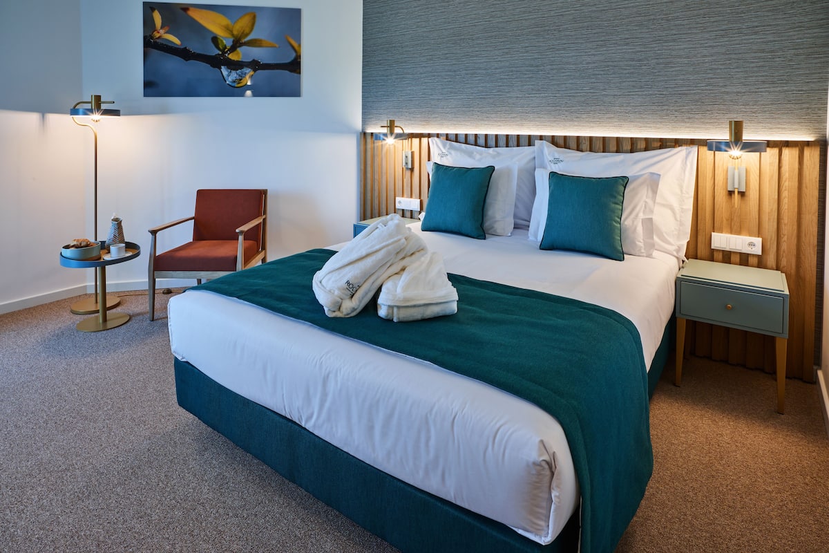A hotel room with a large bed, a chair, a bedside table, and a lamp.
