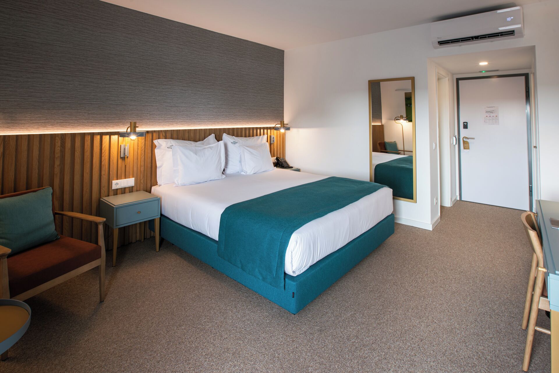 Ein Hotelzimmer mit einem großen Bett, einem Schreibtisch, einem Stuhl, einem Spiegel und einer Tür.