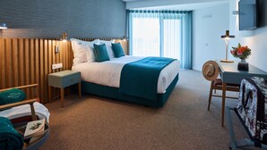 A hotel room with a large bed, a desk, a chair, a TV, and a window with curtains. - Rochavau Hotel (Portimão)
