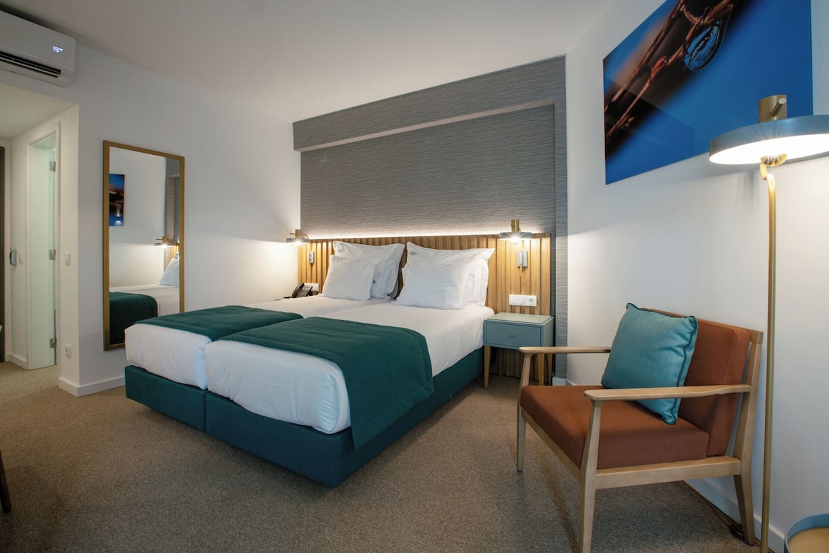 A hotel room with a large bed, a chair, a desk, and a mirror.