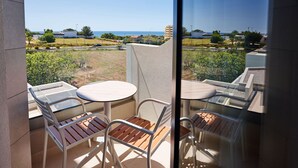 A balcony with a glass table and chairs, a view of the sea, and a building in the background. - Rochavau Hotel (Portimão)