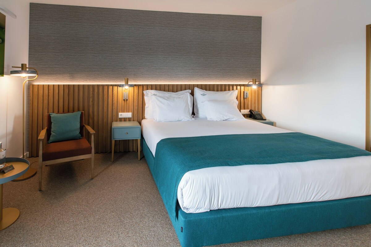 A hotel room with a bed, bedside tables, a nightstand, a lamp, a chair, and a small round table.