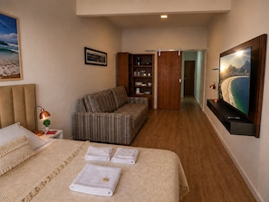 A hotel room with a bed, a sofa, a television, and a bookshelf.