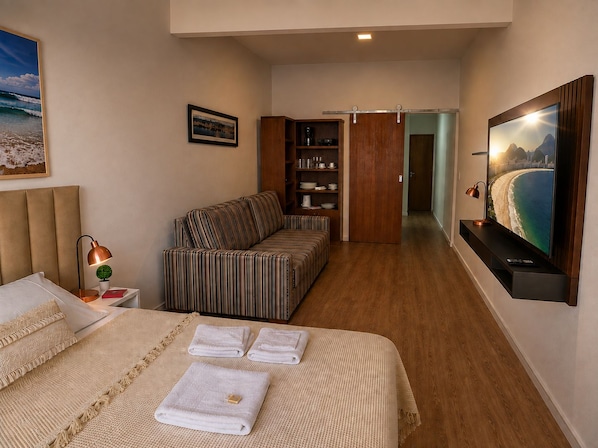 Una habitación de hotel con una cama, un sofá, un televisor y una estantería.