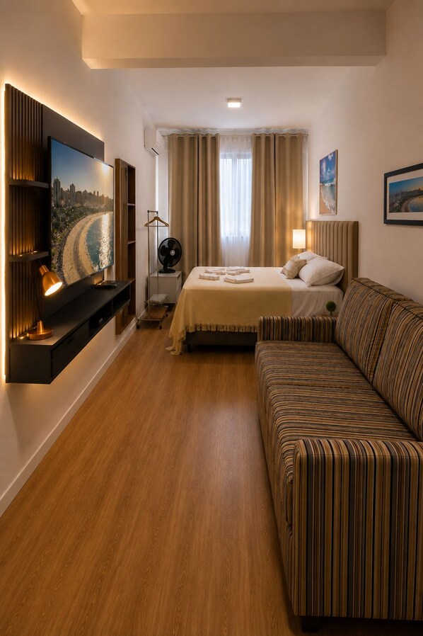 A hotel room with a bed, a sofa, a TV, and a fan.