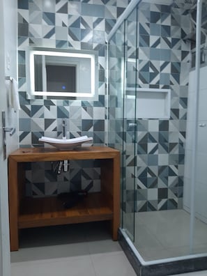 Un baño con pared de diseño geométrico, tocador de madera con lavabo y cabina de ducha de vidrio.