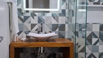 Une salle de bain moderne avec un mur recouvert de carreaux aux motifs géométriques, un meuble-lavabo en bois avec un miroir et une cabine de douche en verre.