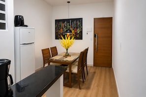 A compact kitchen with a refrigerator, a coffee maker, a dining table with chairs, and a painting above the table.