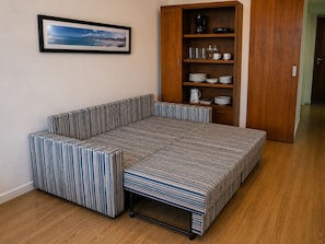 A compact room with a sofa bed, a wooden cabinet with dishes, and a framed picture on the wall.