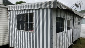 A small, striped, single-room structure with a window and a door, likely a mobile home or a small cabin. - Mobil Home Gère Belesten (Gère-Bélesten)