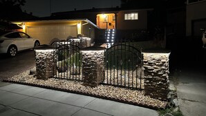 Une maison d’habitation avec un garage, une allée et un mur en pierre surmonté d’un portail en métal.