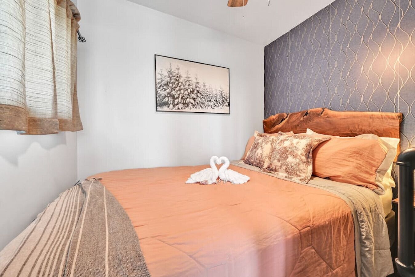 Een slaapkamer met een bed, kussens, een deken, een aan de muur hangend schilderij en een raam met gordijnen.