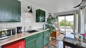 A modern kitchen with green cabinets, a white tiled backsplash, and a large window offering a view of greenery.