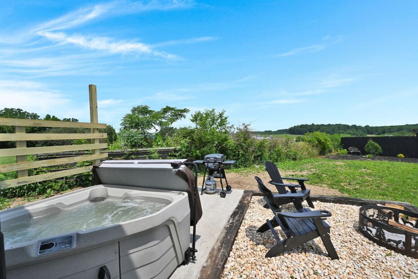 A hot tub, grill, and outdoor seating area with a view of the countryside.