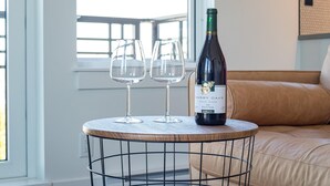 Een ronde tafel met een fles wijn en twee glazen erop, in een kamer met een raam en een beige bank.