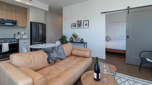 Een moderne woonkamer met een leren bank, een eettafel met stoelen, een keuken met inbouwapparatuur en een slaapkamer met een bed en een schuifdeur.