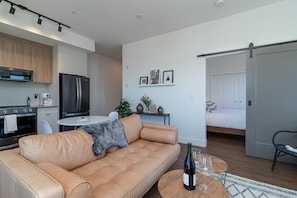 A modern living room with a leather sofa, a dining table with chairs, a kitchen area with appliances, and a bedroom with a bed and a sliding door. - Elegant Retreat in the Heart Old Town Victoria (Victoria)