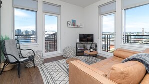 Een moderne woonkamer met een groot raam, een bank, een fauteuil, een televisie en een kleine tafel met een fles.