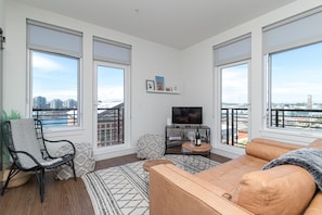 A modern living room with a large window, a sofa, a chair, a TV, and a small table with a bottle. - Elegant Retreat in the Heart Old Town Victoria (Victoria)