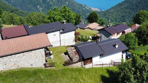 Un ensemble de maisons traditionnelles en pierre et en bois, dotées de toits inclinés, entourées d’une végétation luxuriante et bordées de montagnes, surplombant une vallée et un lac.