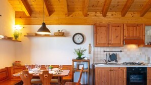 Un coin repas chaleureux, avec une table en bois dressée pour quatre personnes, des chaises en bois, une suspension et une horloge au mur.