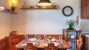 Une table de salle à manger en bois, mise avec des verres à vin et des assiettes, une horloge au mur et un luminaire suspendu.