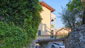 A stone wall with ivy, a building with a balcony, and parked cars. - Apartment Bot by Interhome (Gravedona)