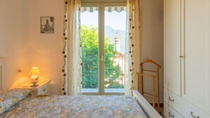 A bedroom with a bed, a nightstand with a lamp, a wardrobe, and a window with curtains. - Apartment Bot by Interhome (Gravedona)