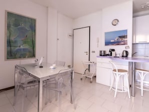 Una habitación moderna y minimalista con una mesa de comedor y sillas, una pequeña kitchenette y un cuadro en la pared.
