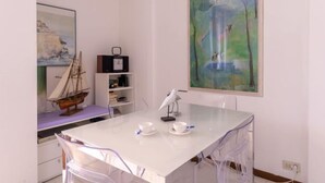 Ein Zimmer mit einem weißen Tisch, Stühlen, einem Gemälde, einem Bücherregal und einem Schiffsmodell.
