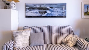 Ein gestreiftes Sofa mit Kissen, ein gerahmtes Bild von einem Meeresblick und eine Lampe auf einem Schrank.