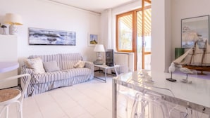 Ein modernes Wohnzimmer mit einem gestreiften Sofa, einem Glastisch und einem Essbereich mit einem Schiffsmodell.