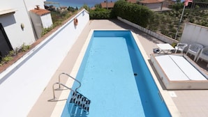 Ein rechteckiger Swimmingpool mit einer Metallleiter, umgeben von einer weißen Mauer und einem Metallzaun.