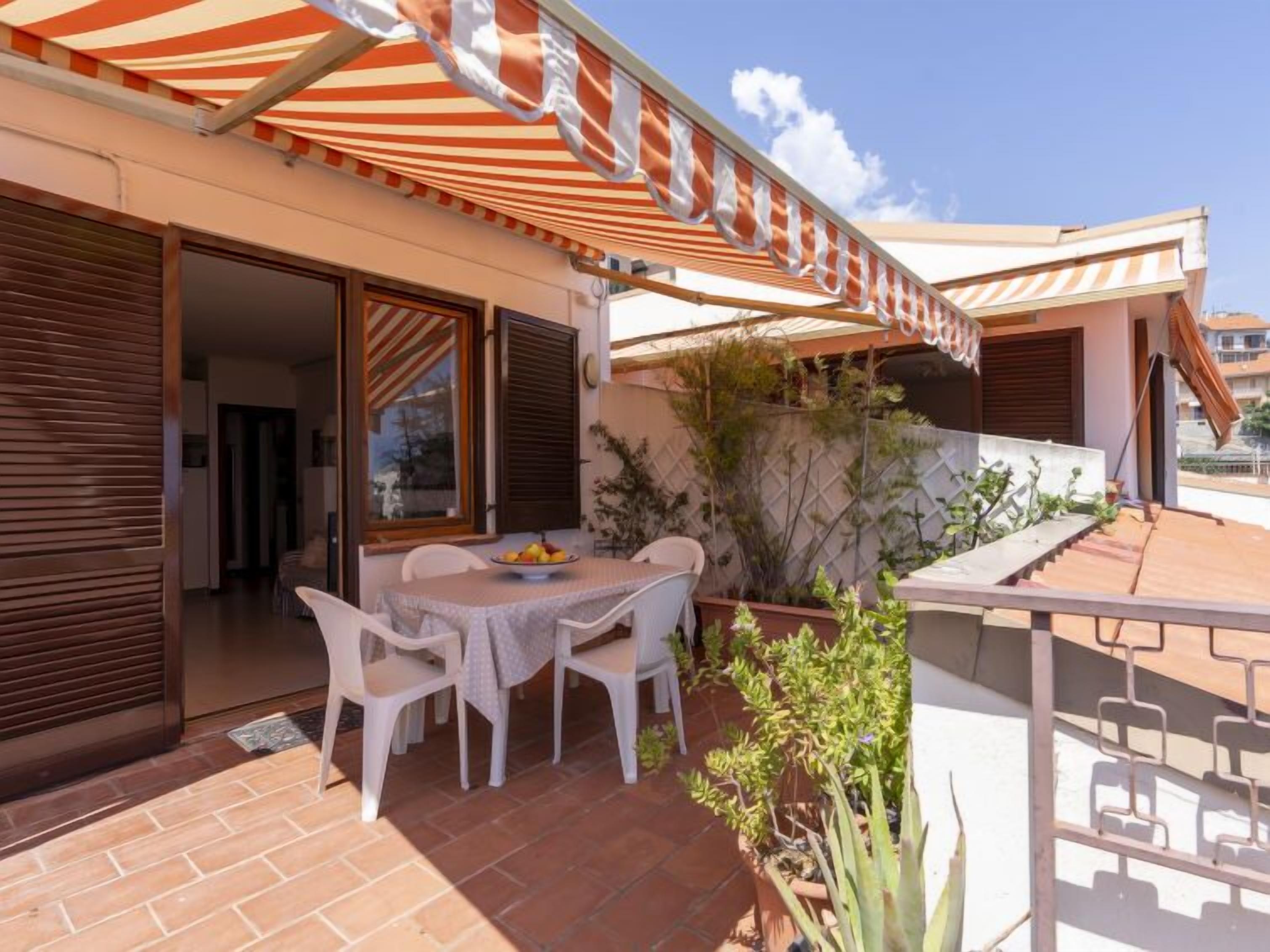 An outdoor patio with a table and chairs, a striped awning, and a view of the surrounding area.