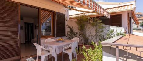 An outdoor patio with a table and chairs, a striped awning, and a view of the surrounding area.