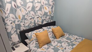 A bedroom with a bed, two pillows, a bedside table with a lamp, and a blanket.