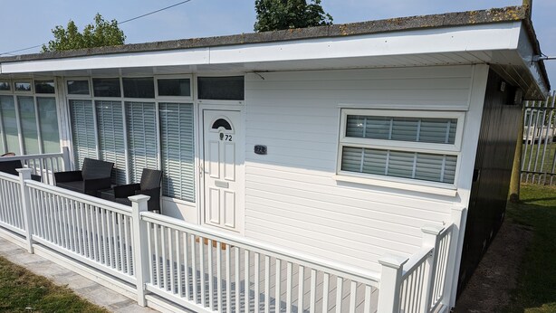 A white mobile home with a porch, number 72, featuring a small seating area with chairs and a table.