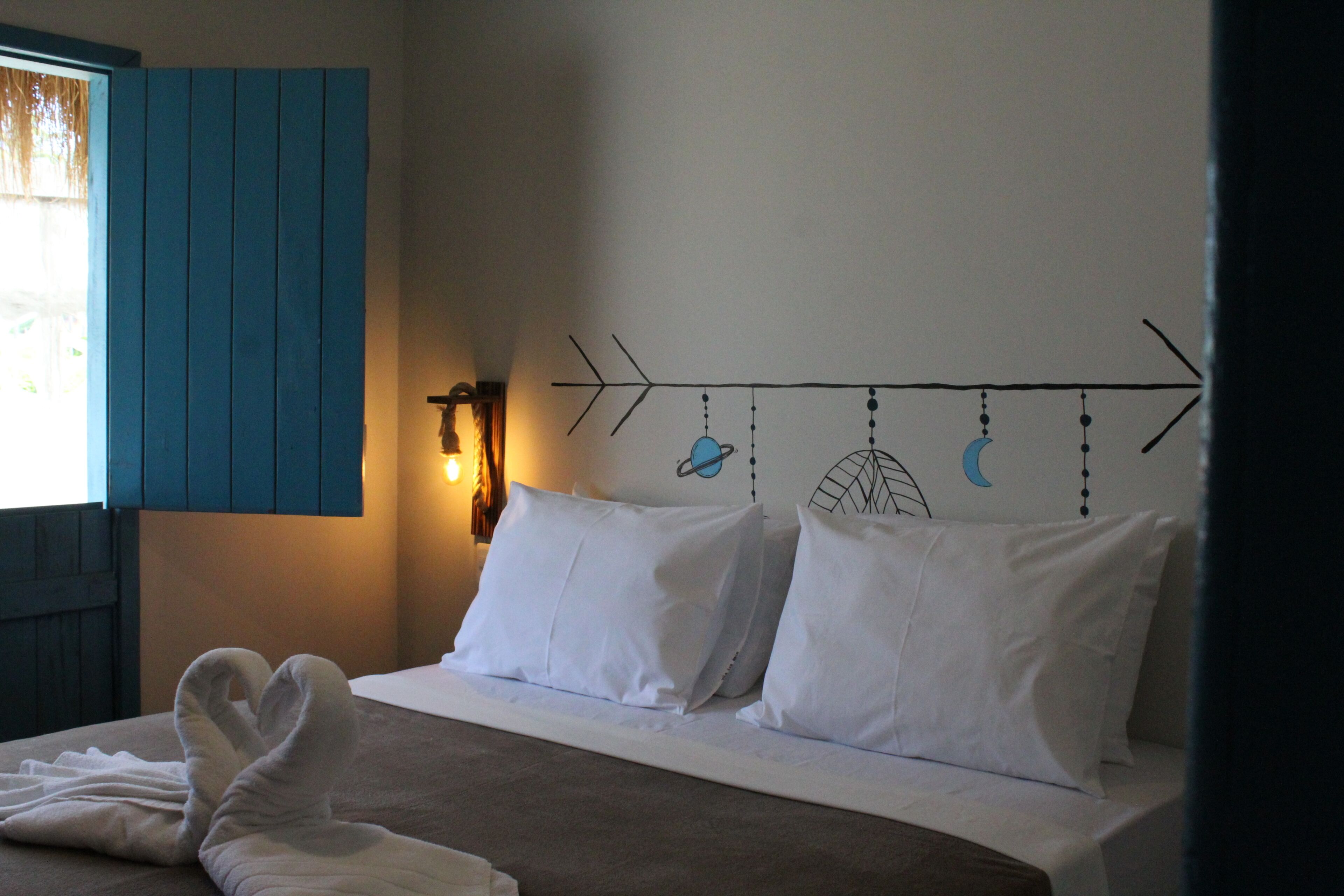 Ein Bett mit weißen Kissen und einem Handtuch, eine Wand mit einem Halbmond- und Sterndruck sowie ein Fenster mit blauen Rollläden.