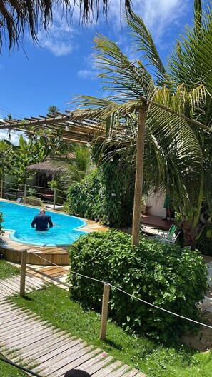Une piscine entourée d’une végétation luxuriante, notamment de palmiers et d’une structure à toit de chaume.