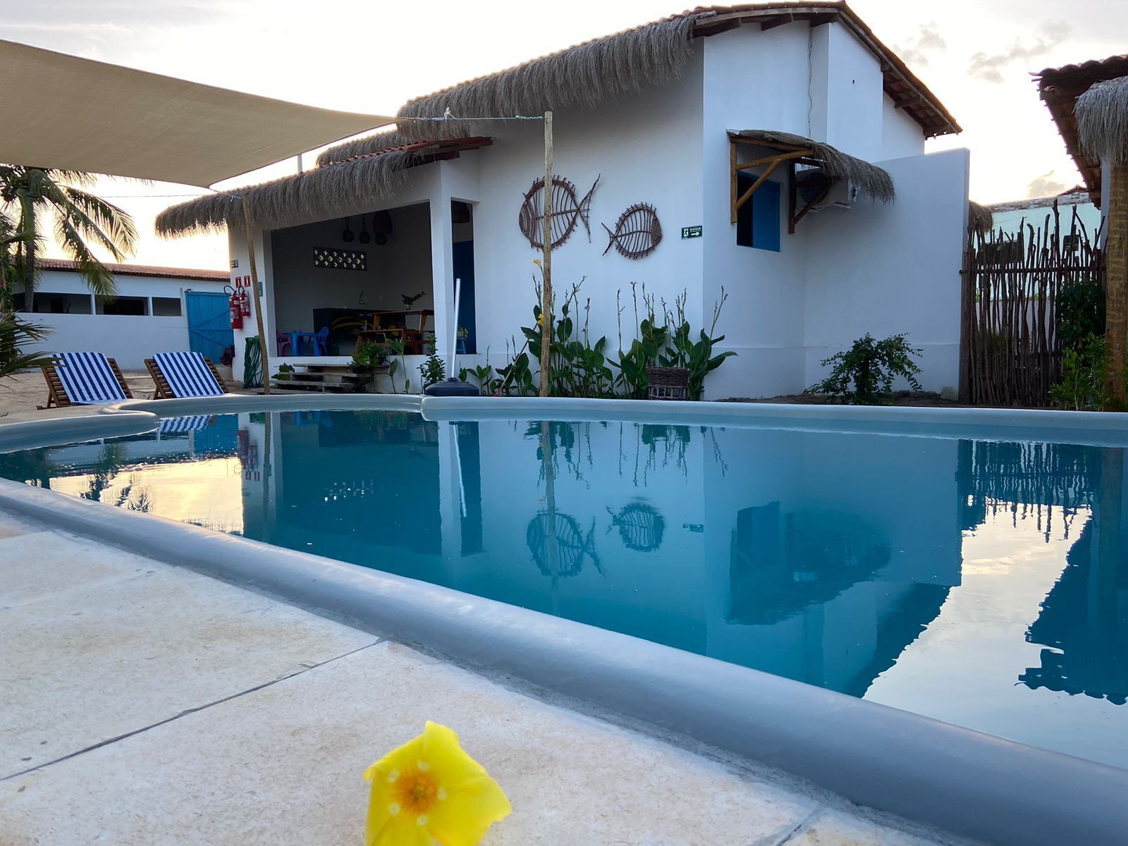 A poolside area with a clear blue pool, a thatched-roof building, and two lounge chairs.